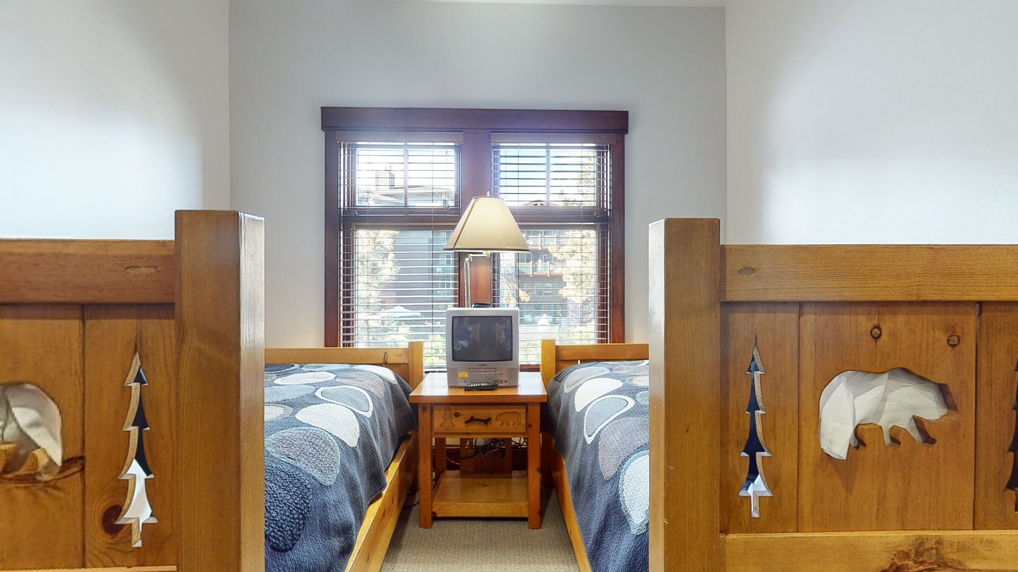 Een kamer met twee houten bedden, een bureau met lamp en een raam met zonwering.