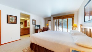 A hotel room with a large bed, a desk with a lamp, a TV, and a view of the outside.