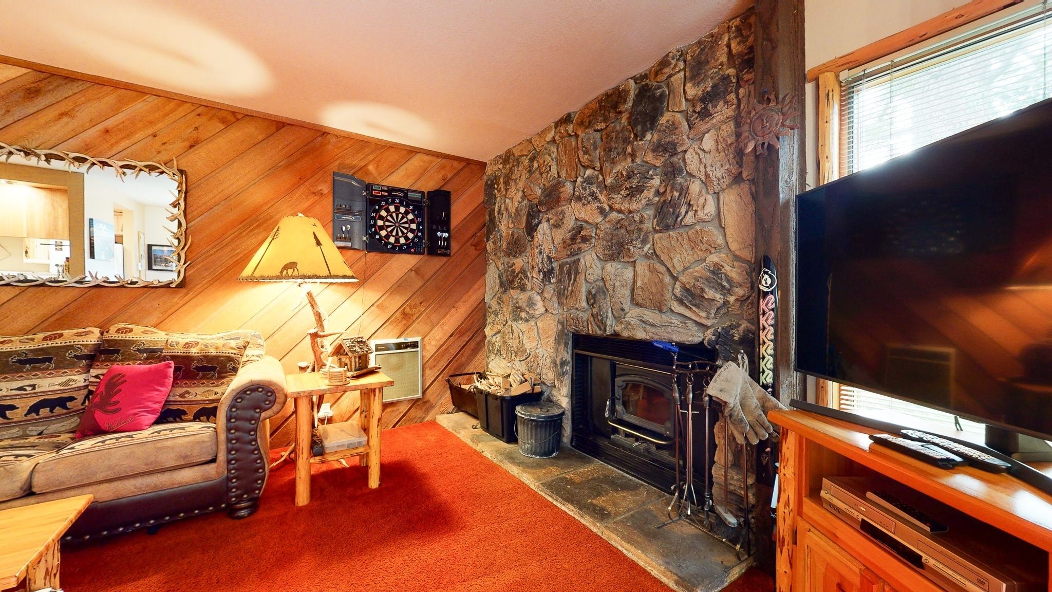 Una sala de estar acogedora con chimenea de piedra, televisión y pared de madera.