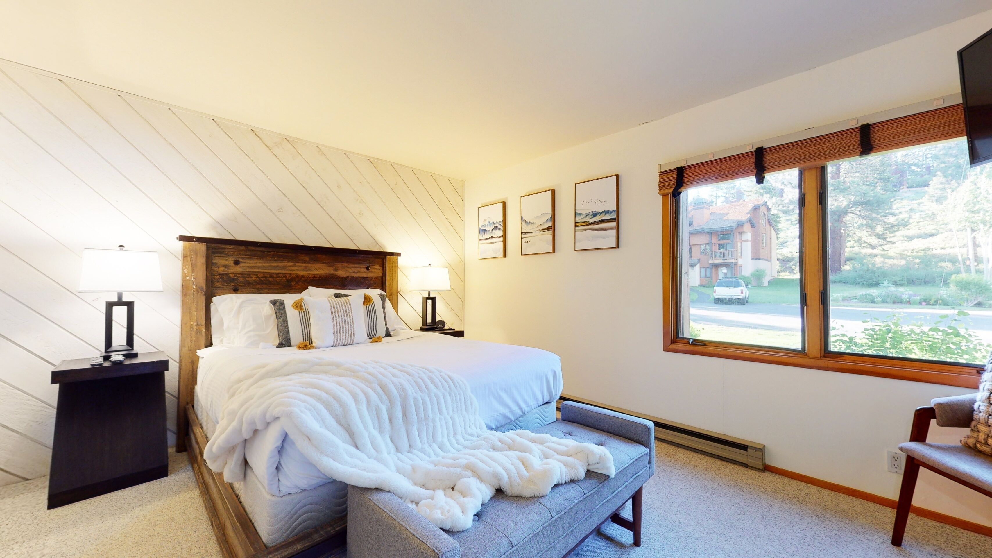 A bedroom with a bed, bedside tables, a bench, and a window with a view of a building and trees.