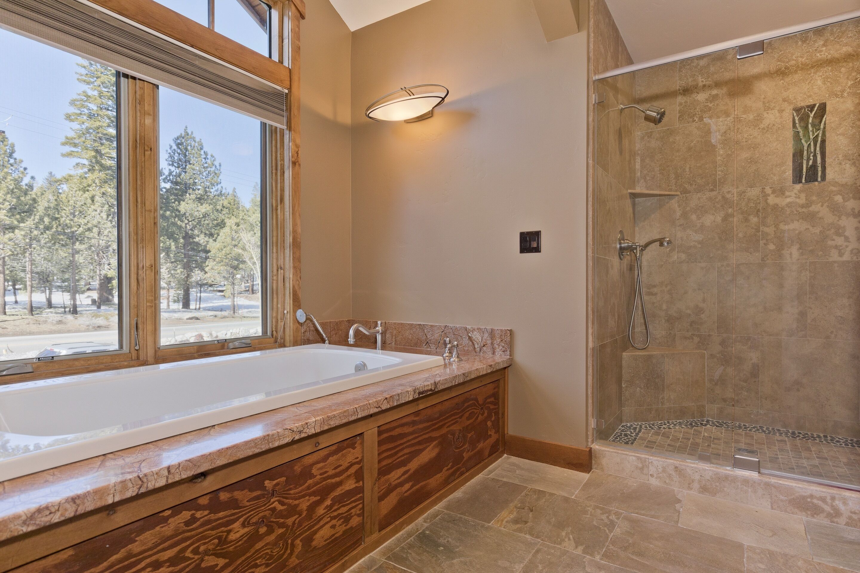 A bathroom with a large bathtub, a shower, and a window with a view of trees.