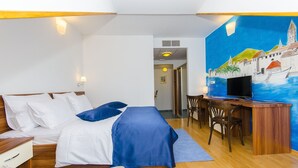 A hotel room with a bed, desk, and a painting of a coastal scene. - Palma Rooms B&B (Split)