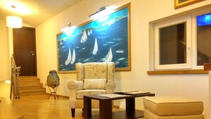 A living room with a large painting of sailboats, a sofa, a coffee table, and a small statue. - Palma Rooms B&B (Split)