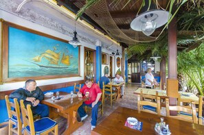 Un restaurante con mesas y sillas de madera, un gran mural de un barco velero y luces colgantes.