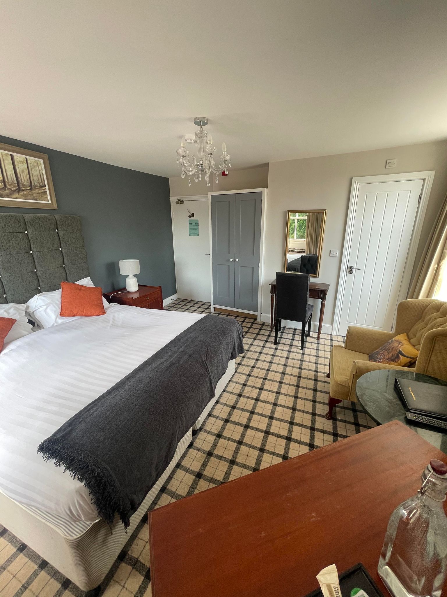 Een hotelkamer met een bed, een bureau, een stoel, een bank, een kroonluchter en een deur.