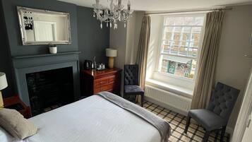 Ein Hotelzimmer mit einem großen Bett, einem Kamin, einem Spiegel, einer Chandelüster, einem Fenster mit Vorhängen und einem Schachbrettboden.