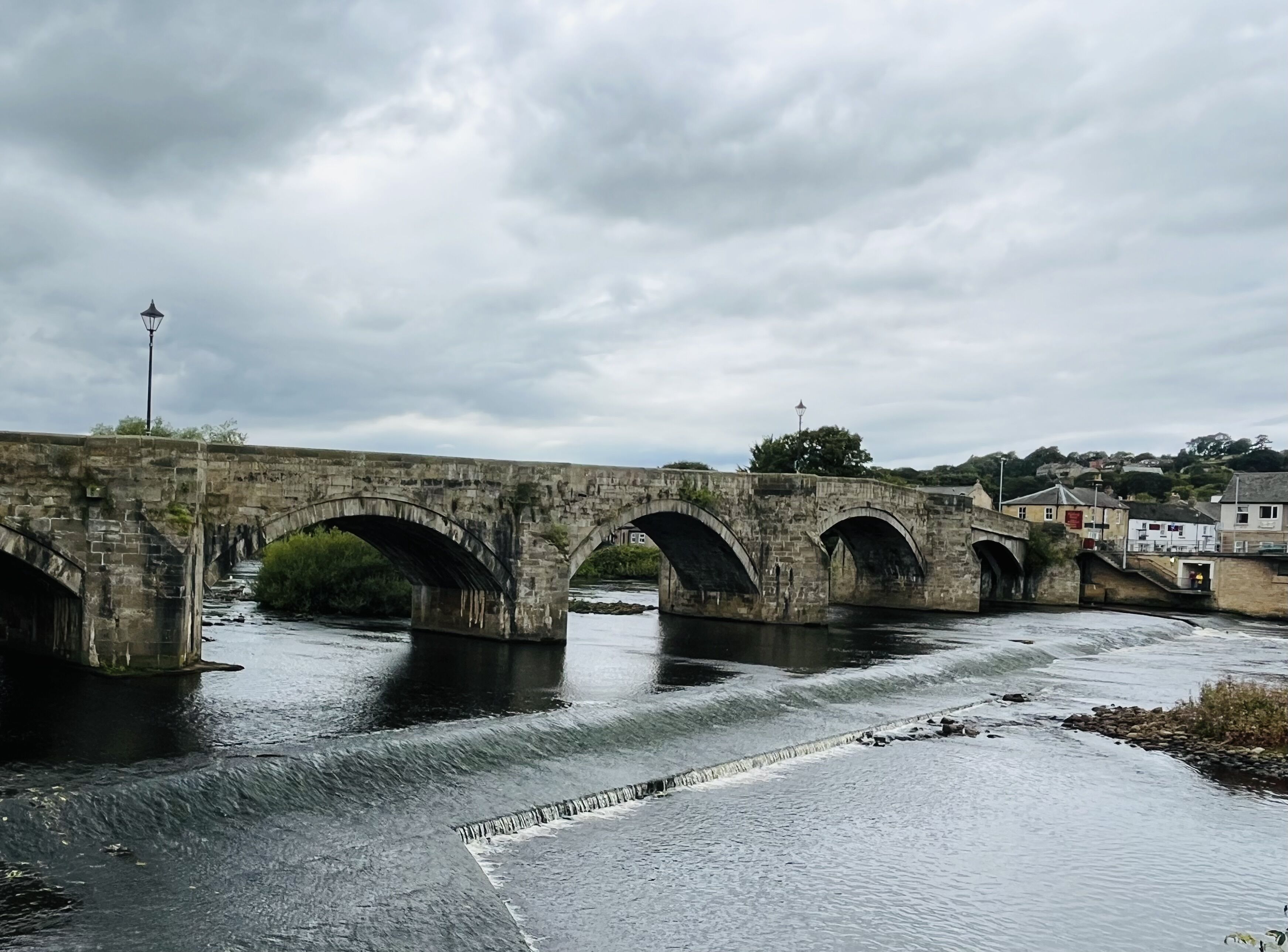 A stone bridge over a river with a town in the background.