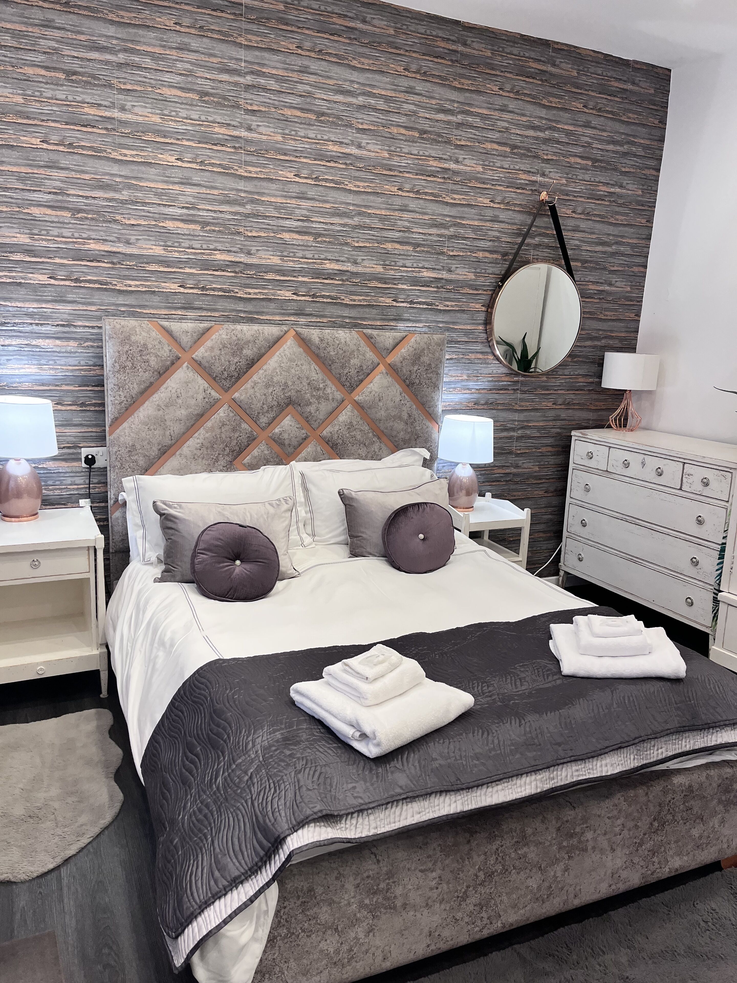 A modern bedroom with a bed, nightstands, a dresser, and a mirror.