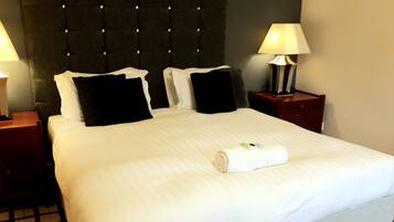A neatly made bed with white linens, two black pillows, and a rolled towel on the bed. There are two bedside tables with lamps on either side of the bed.
