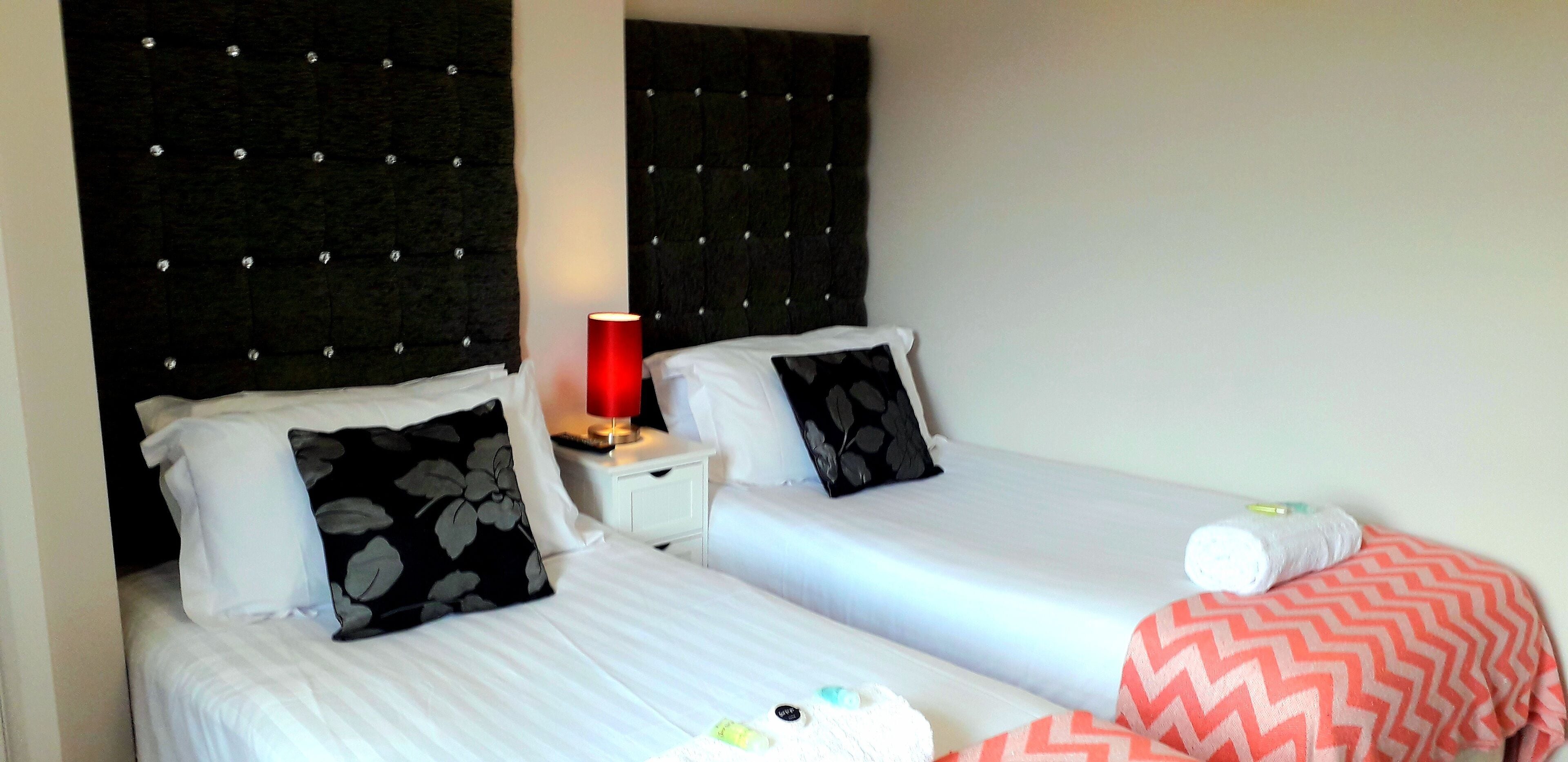 Two single beds with black and white floral pillows, a red lamp on a bedside table, and a pink chevron-patterned blanket.