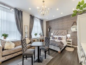 A modern living room with a sofa, dining table, and a bed with a tufted headboard. - The Railway Hotel (Hexham)