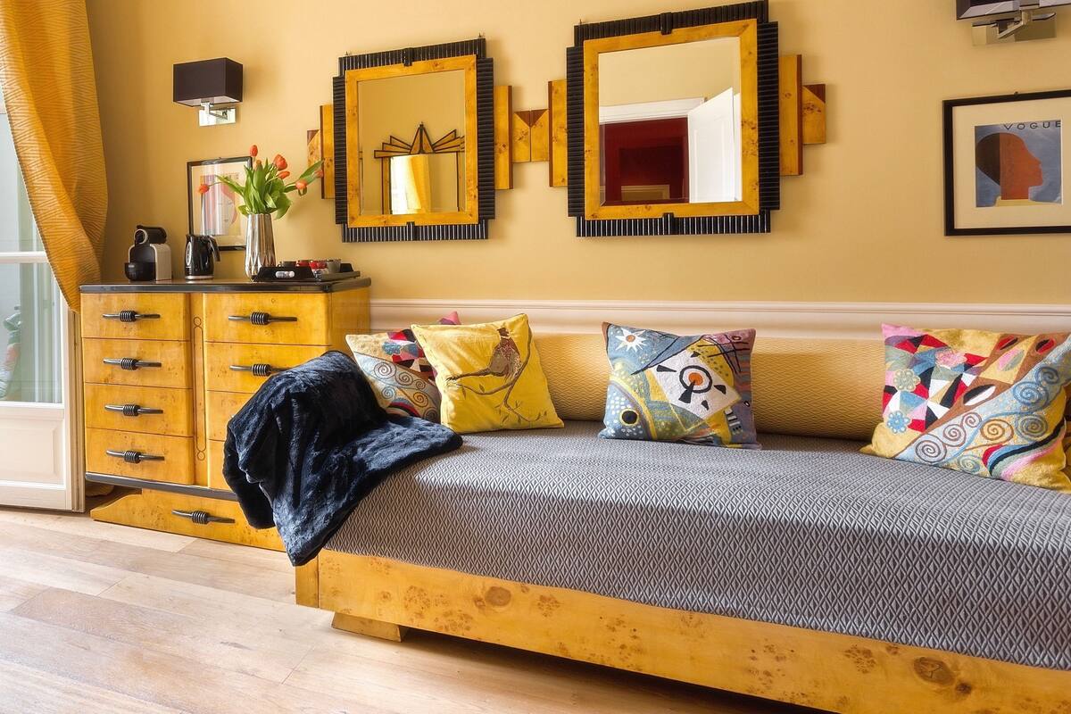 A bedroom with a bed, a wooden dresser, a lamp, and a mirror.