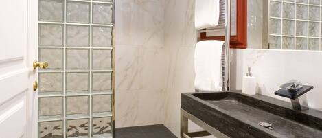 A modern bathroom with a glass shower enclosure, a marble-tiled floor, a dark granite countertop, and a large mirror with a red frame.