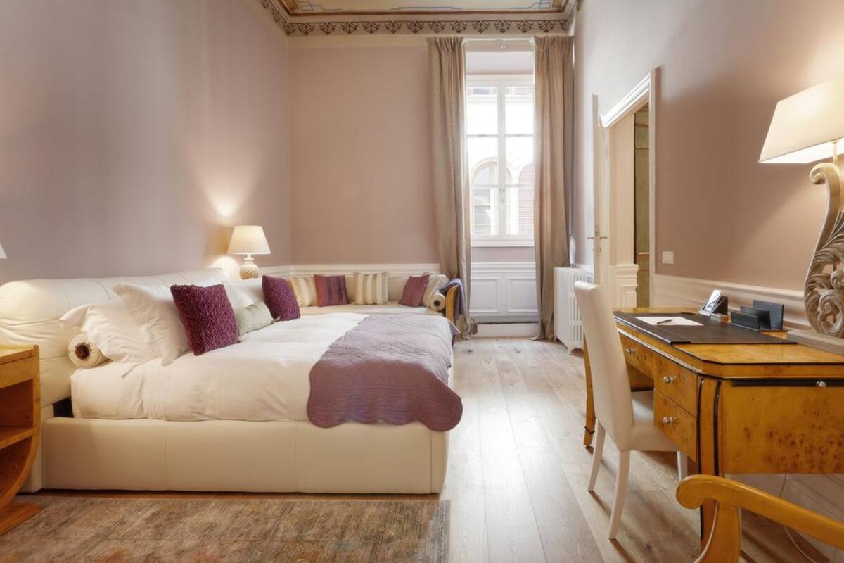 A hotel room with a large bed, bedside lamps, a wooden desk, and a mirror.