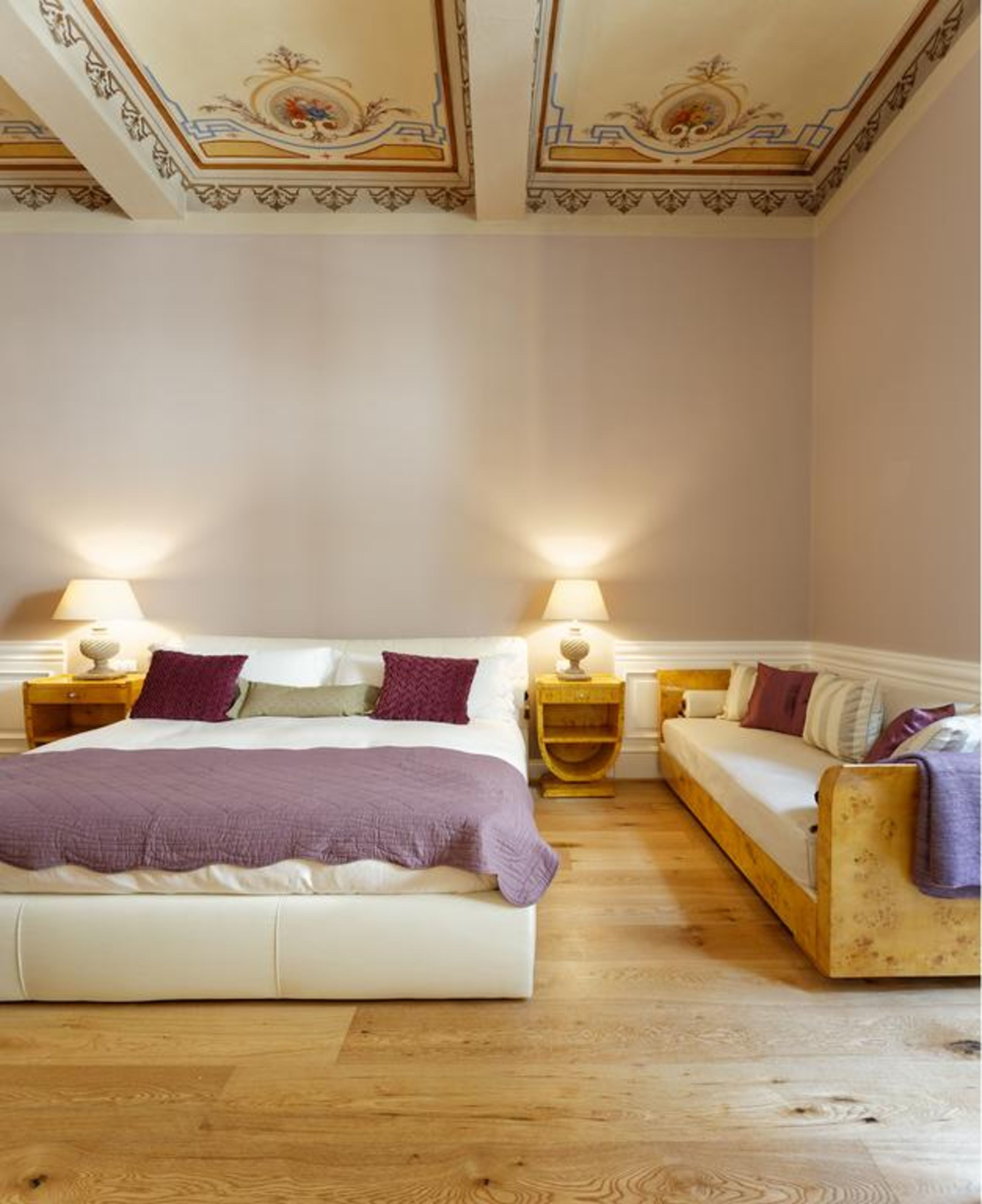 Een slaapkamer met een bed, een sofa, twee nachtkastjes en een decoratief plafond.