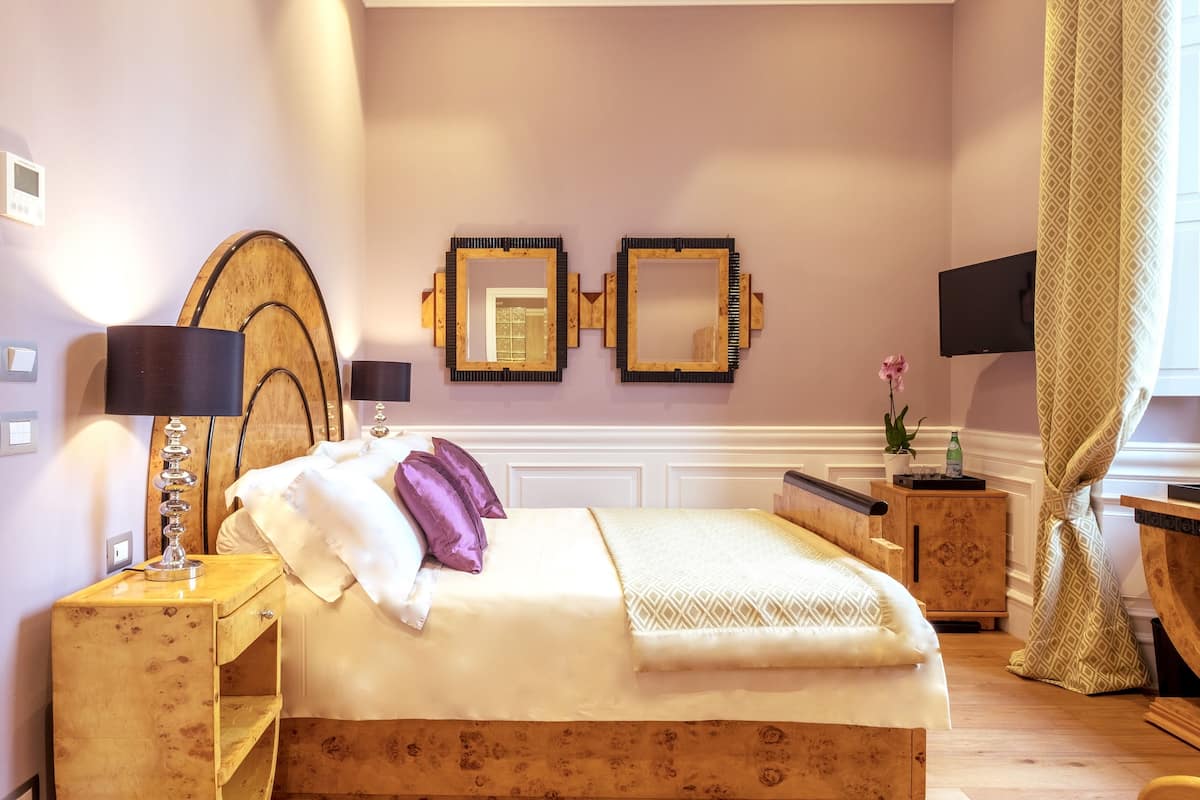 A bedroom with a wooden bed, two bedside tables, a mirror, a TV, and a window with curtains.