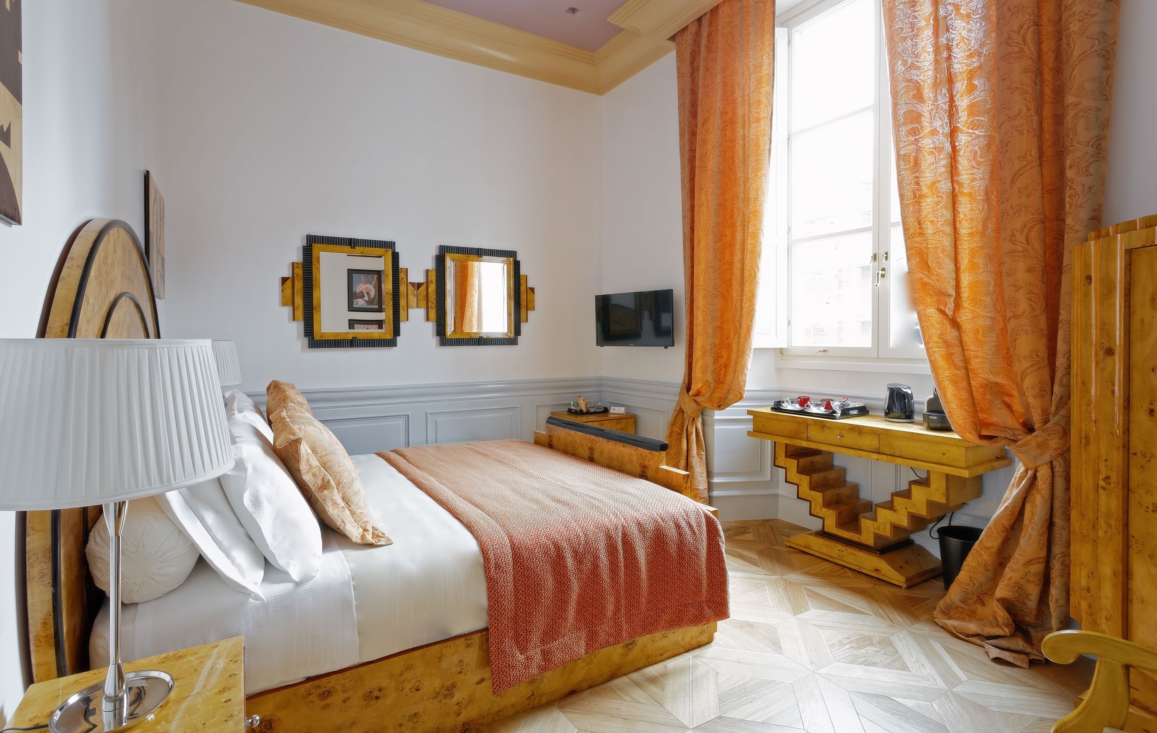 A bedroom with a bed, bedside table, lamp, and a wooden desk with a chair.