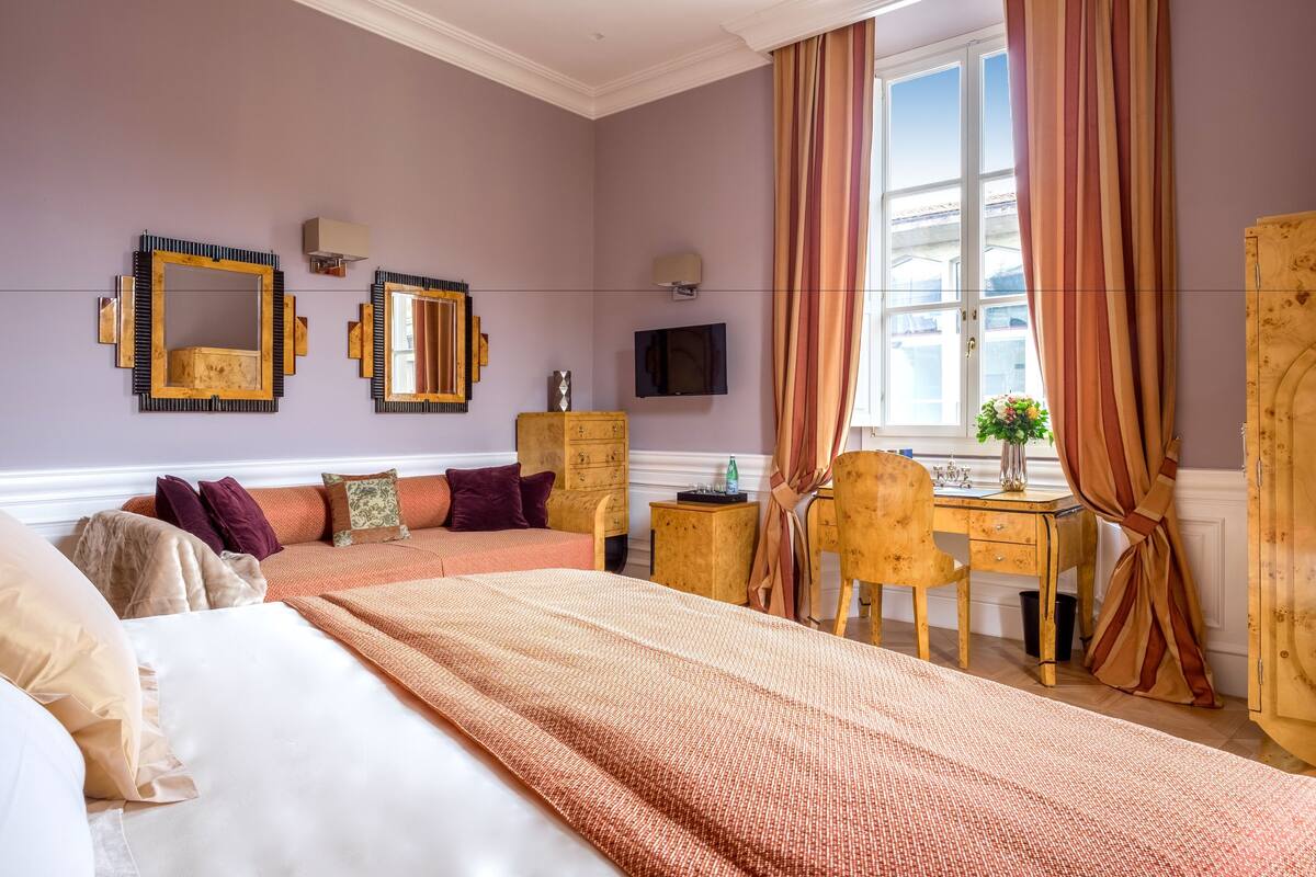 A bedroom with a large bed, a wooden desk, a dresser, and a television on the wall.