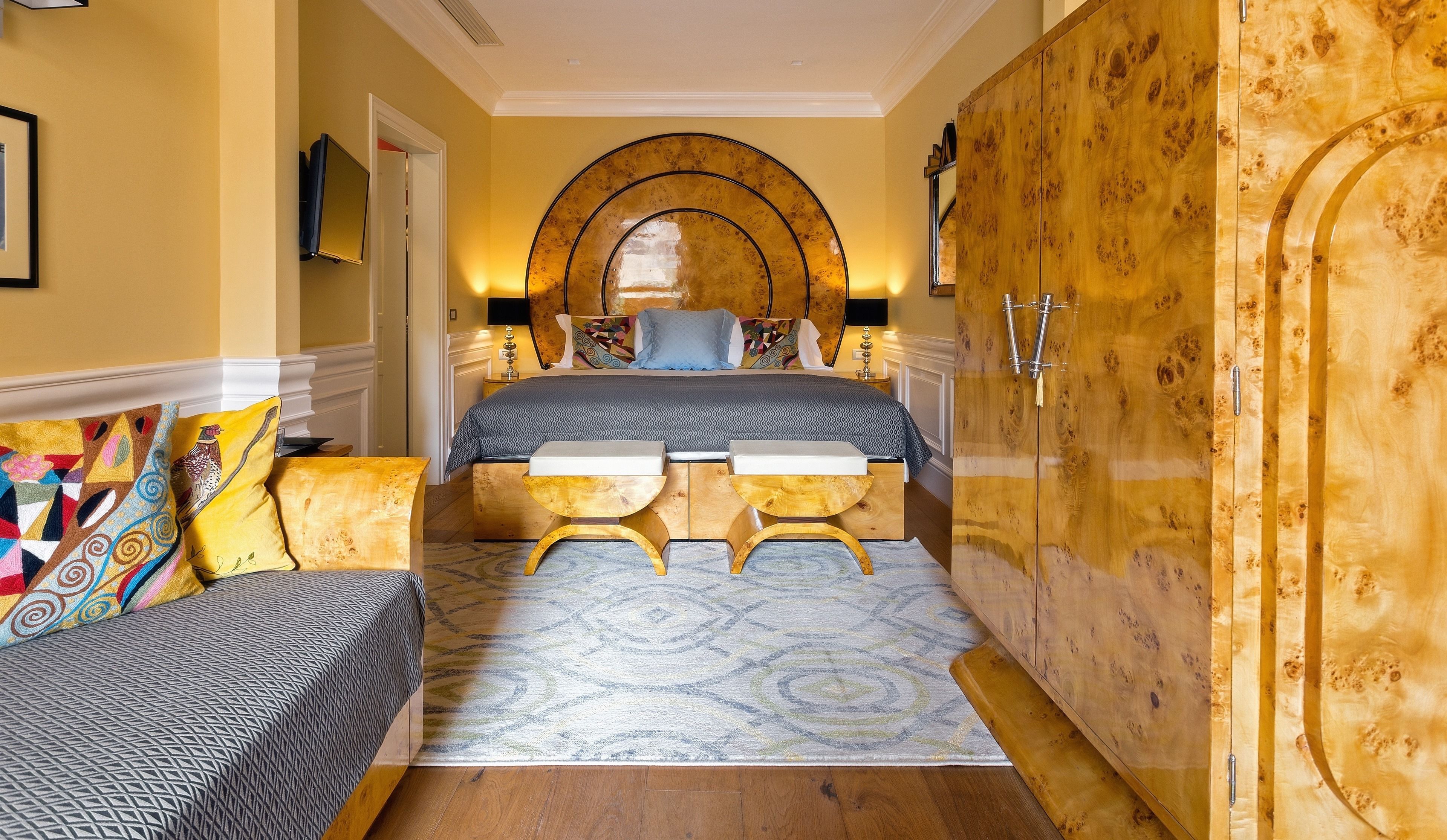 Une chambre d’hôtel avec un lit, une armoire en bois, une petite table et un tapis à motifs.