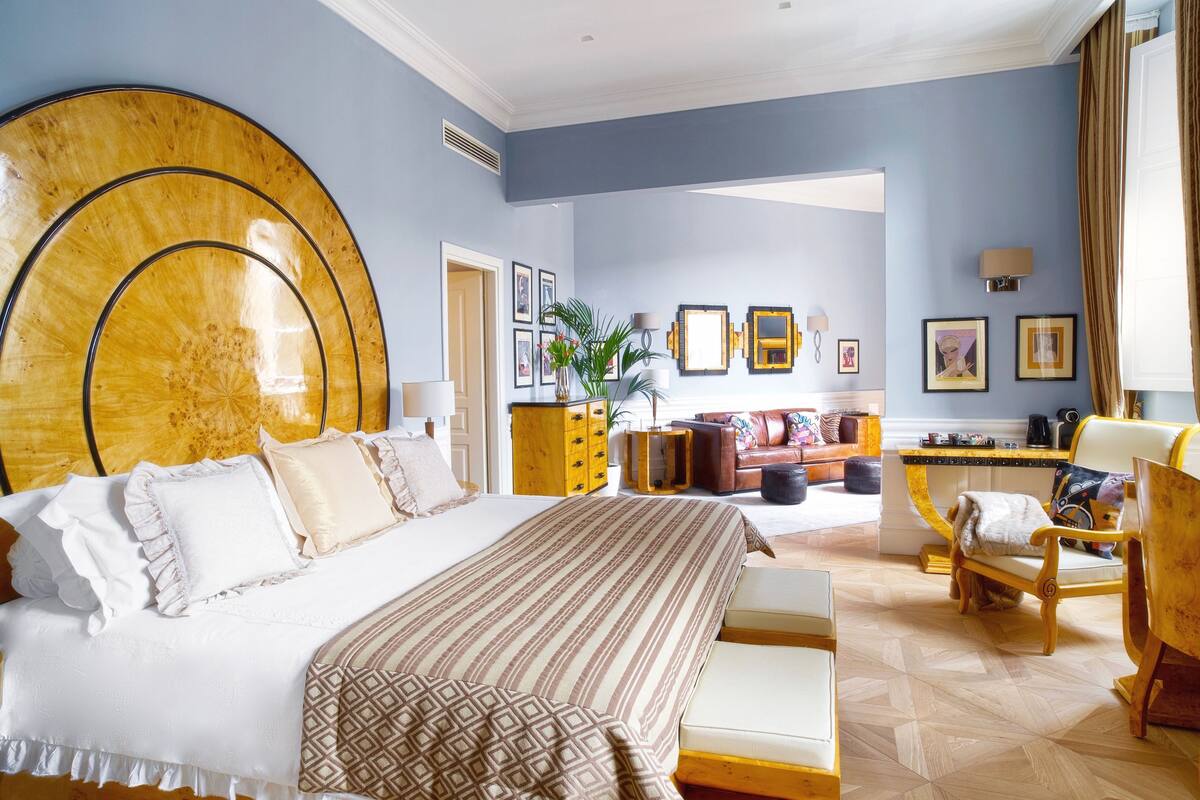 A spacious hotel room with a large bed, a sitting area with a sofa and armchairs, and a dining area with a table and chairs.