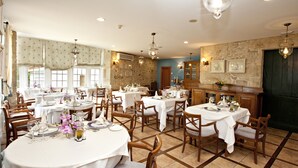 A dining area with round tables, wooden chairs, and a stone wall. - Termas de Cuntis Hotel Castro do Balneario (Cuntis)