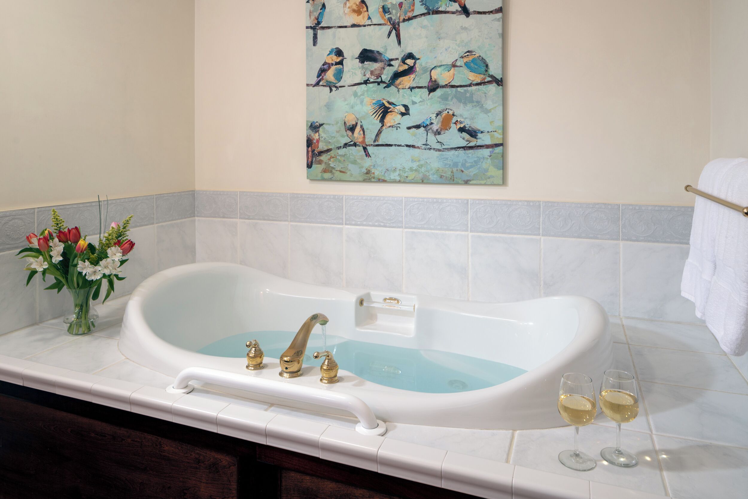 Ein Badezimmer mit einer Badewanne, einem Blumenstrauß und einem Vogelgemälde an der Wand.