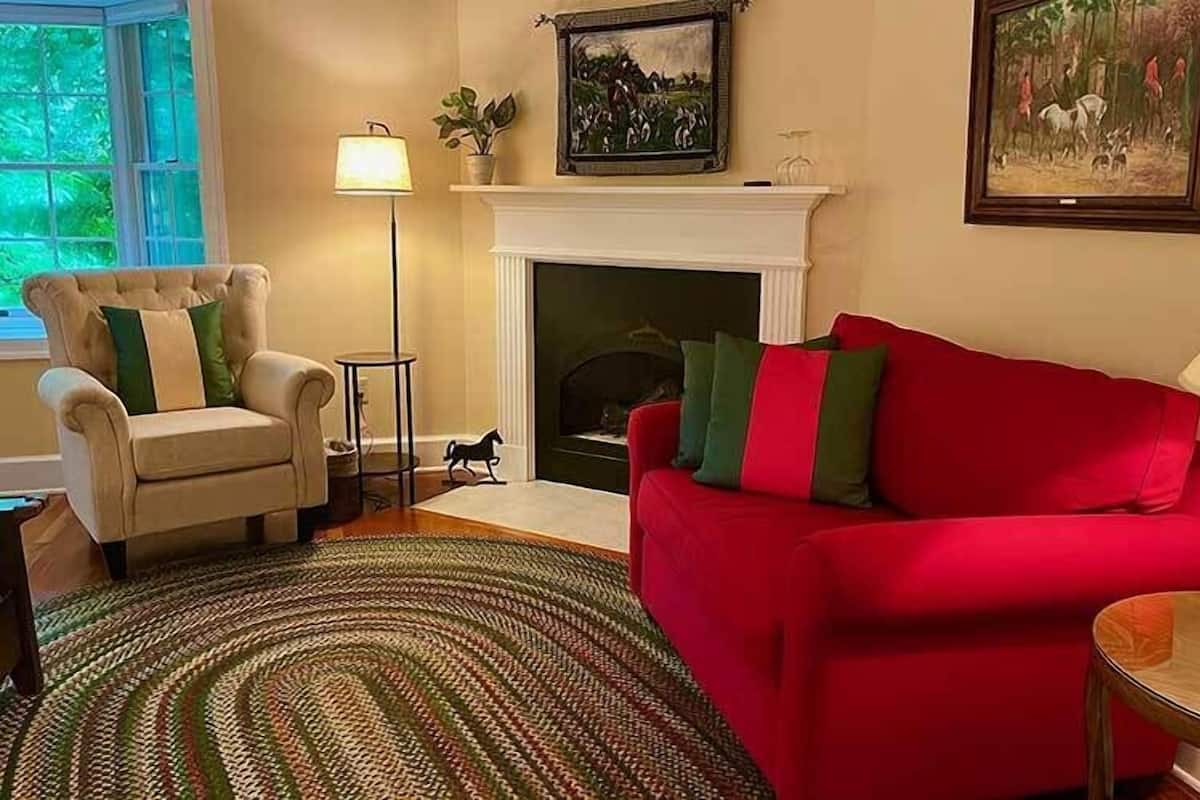 A living room with a fireplace, a red sofa, a white armchair, and a patterned rug.