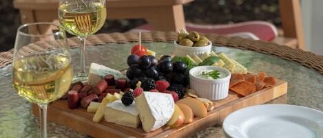 A glass table with a cheese board, grapes, olives, and a bowl of dip. Two glasses of white wine are also visible.