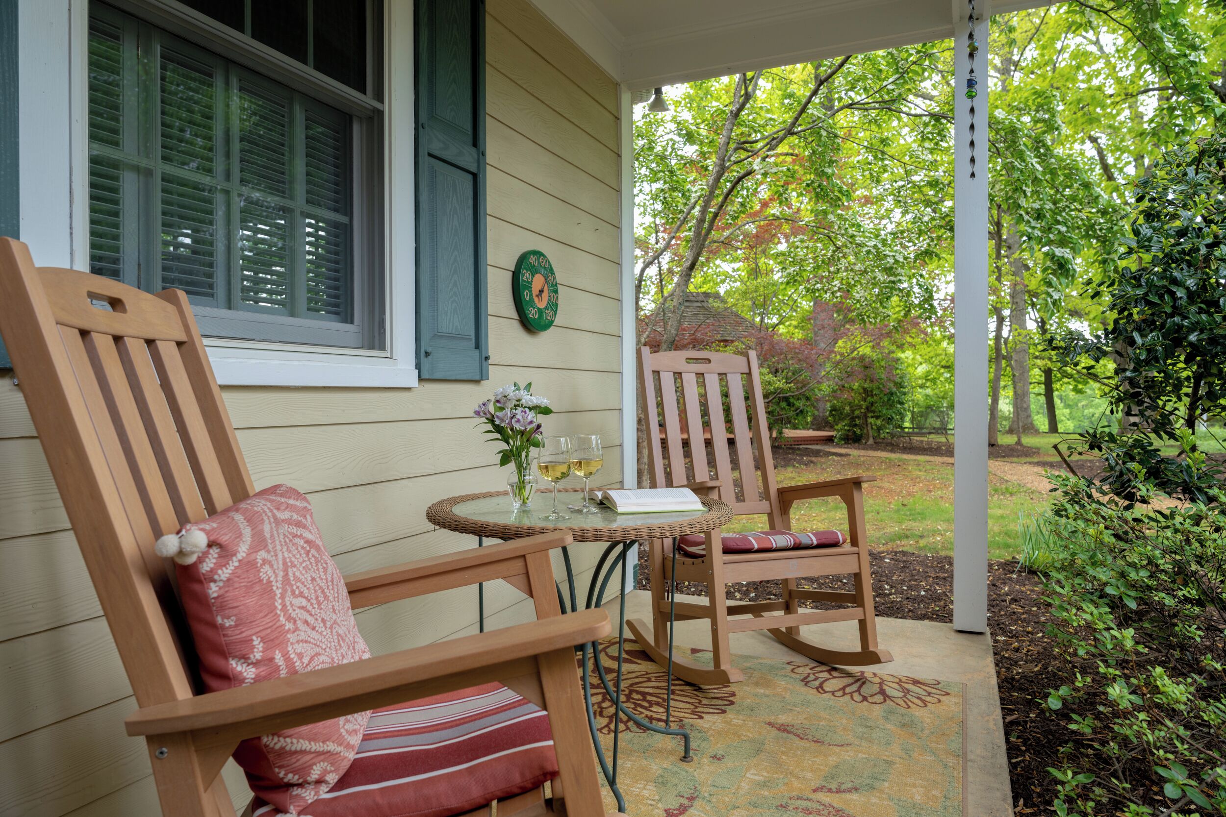 A porch with two wooden rocking chairs, a small round table with a glass top, and a green wall clock.
