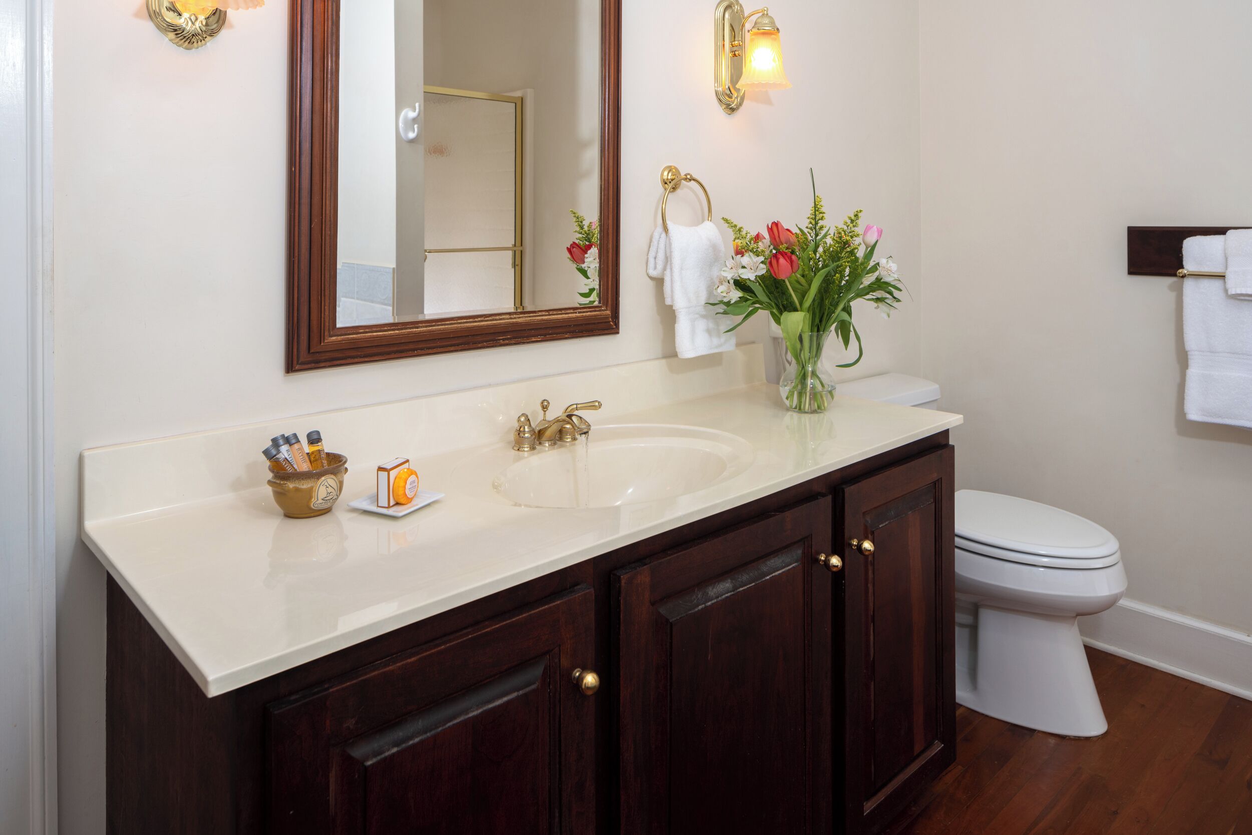 A bathroom with a white sink, dark wooden cabinets, a mirror, a toilet, and a vase with flowers.