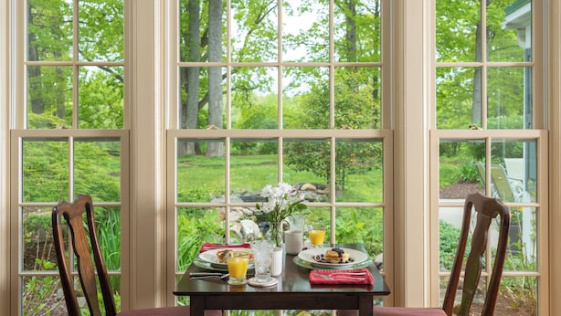 Une table à manger avec des aliments pour le petit-déjeuner, deux chaises et une fenêtre donnant sur un paysage verdoyant.
