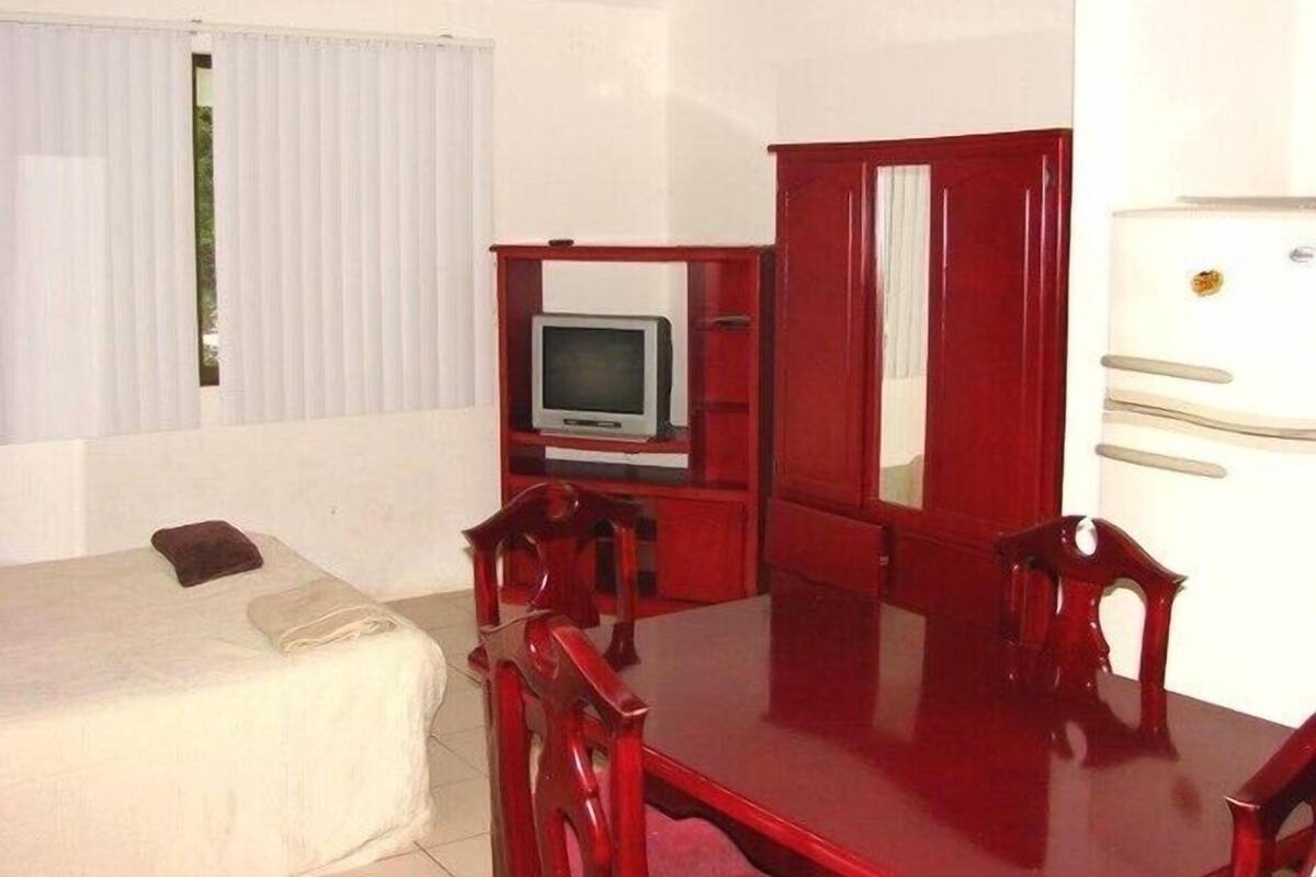 Una habitación pequeña y funcional con cama, televisión, mueble de madera y una mesa.