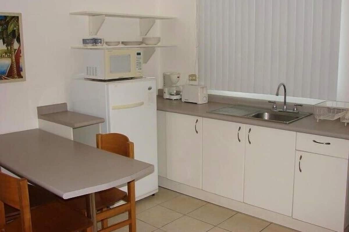 Cocina compacta con refrigerador, microondas, tostadora, pileta y comedor con mesa y sillas.