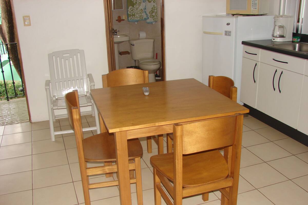 Una cocina pequeña con una mesa y sillas de madera, un refrigerador y un lavamanos.