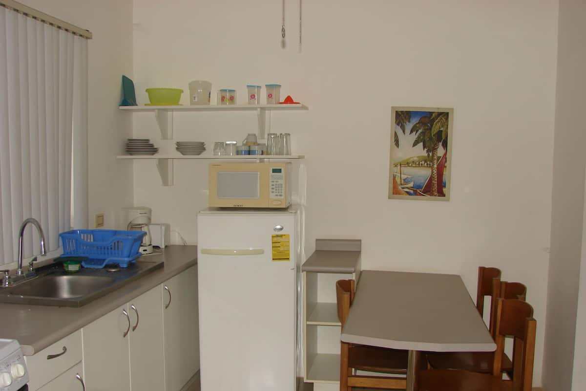Una cocina compacta con armarios blancos, un microondas, un refrigerador, un lavamanos y una mesa de comedor con sillas.