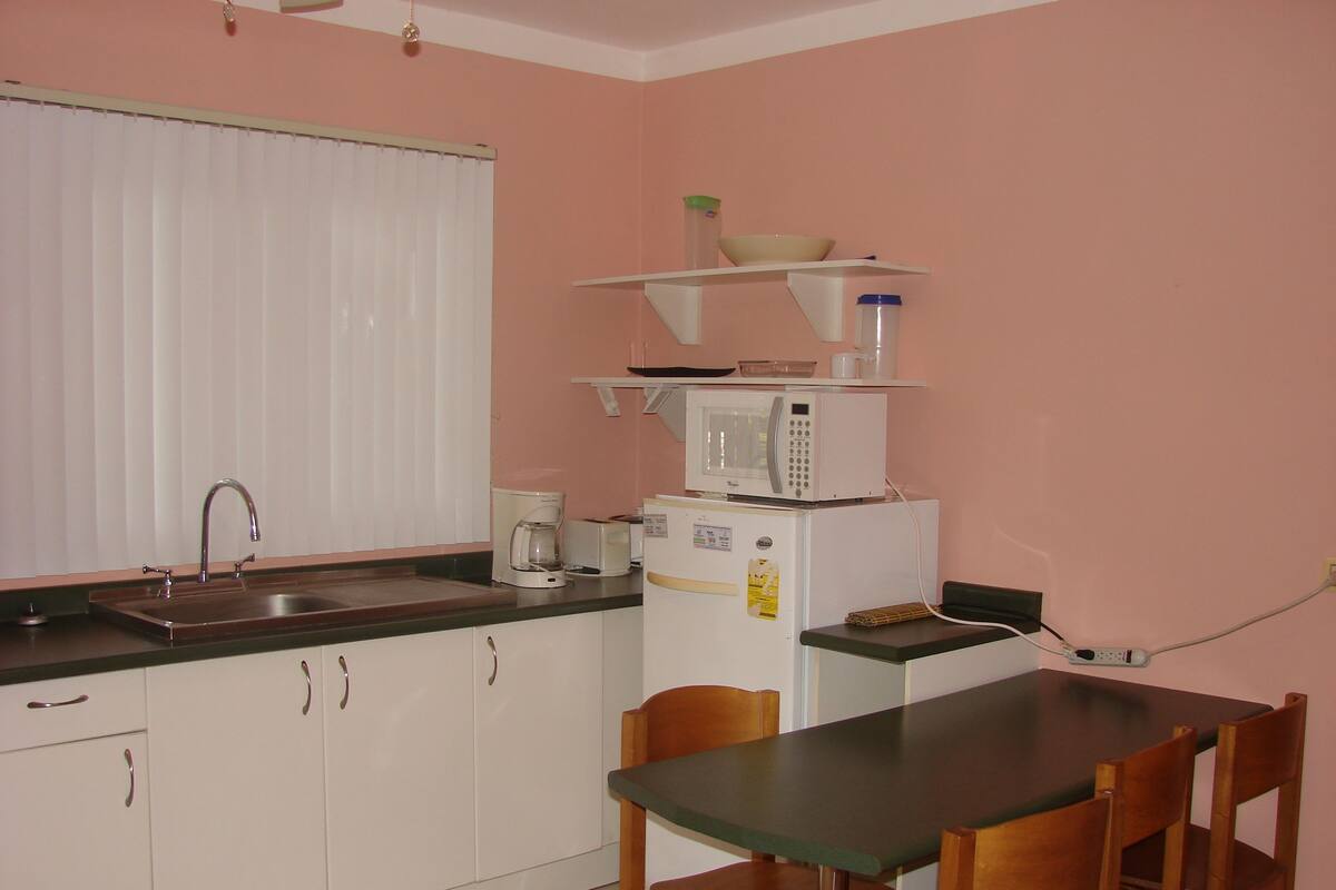 Cocina compacta con lavamanos, microondas, cafetera y refrigerador. Hay una mesa de comedor con sillas.