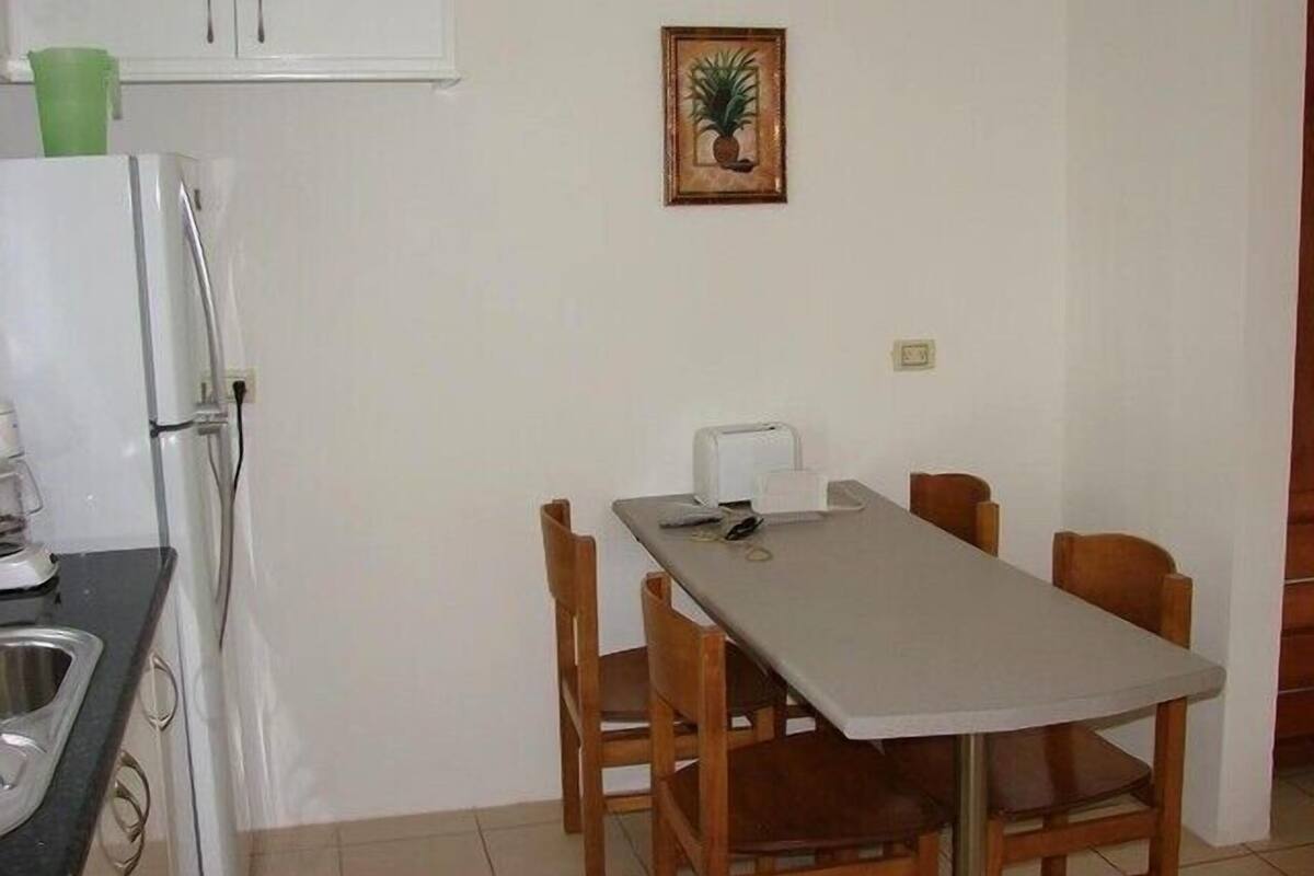 Una pequeña cocina con refrigerador, tostadora y una mesa de comedor con sillas.