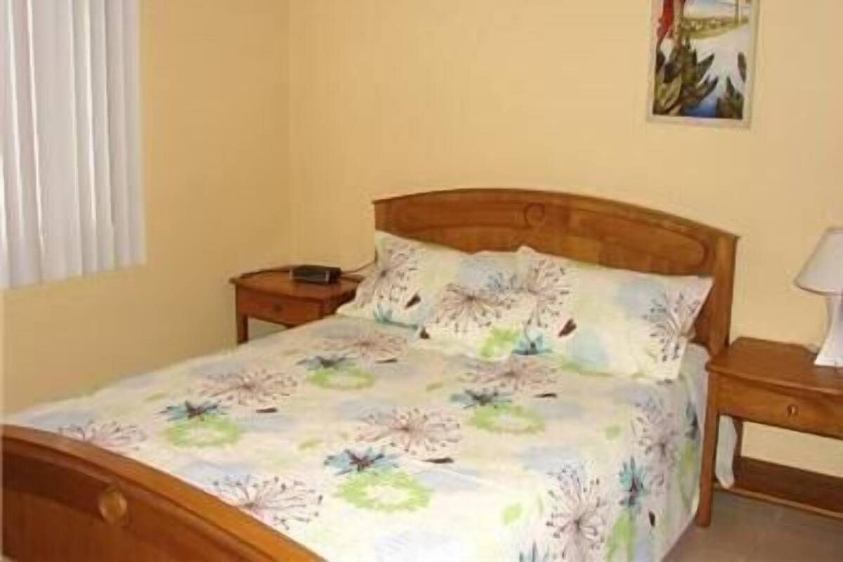 Un dormitorio con cama de madera, una mesita de noche y un cuadro colgado en la pared.