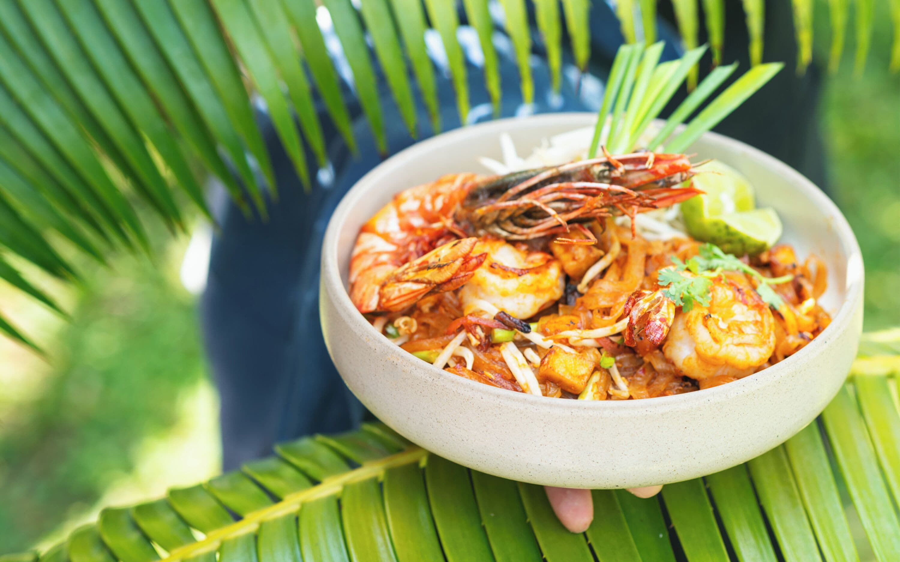 A bowl of shrimp dish with lime and cilantro garnish, placed on a palm leaf.