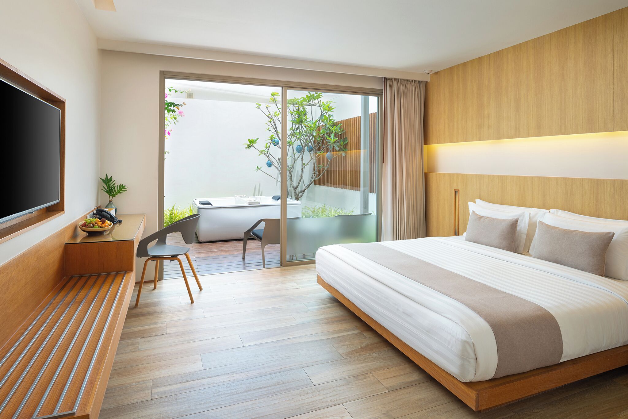 Una habitación de hotel moderna con una cama grande, un escritorio con una silla, un televisor y un ventanal corredero a un balcón.