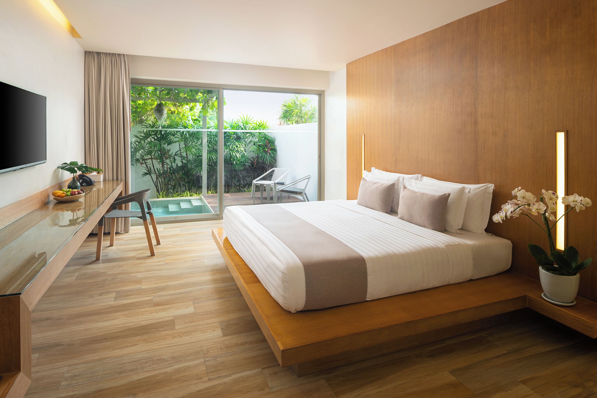 Un dormitorio moderno con cama, escritorio, televisor y balcón con plantas.