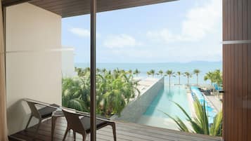 Un balcón con vistas a una piscina y palmeras, con vista al mar.