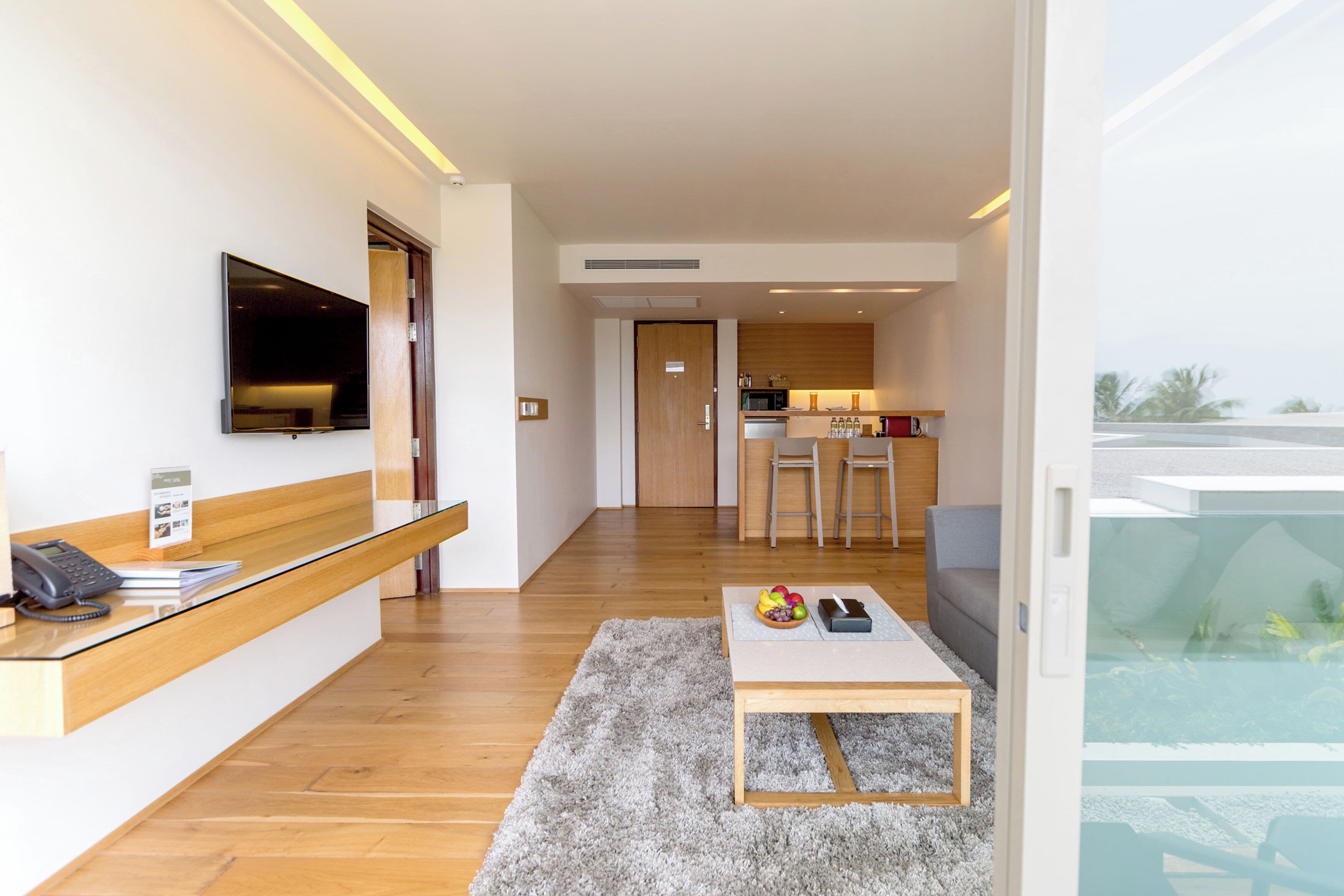 Un hall d’hôtel moderne comprenant un comptoir d’accueil, un téléviseur à écran plat, un coin cuisine et un espace salon avec une table et des chaises.