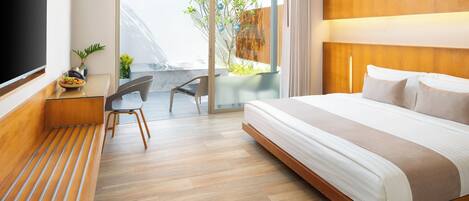 A modern hotel room with a large bed, a flat-screen TV, a desk with a chair, and a balcony with plants.