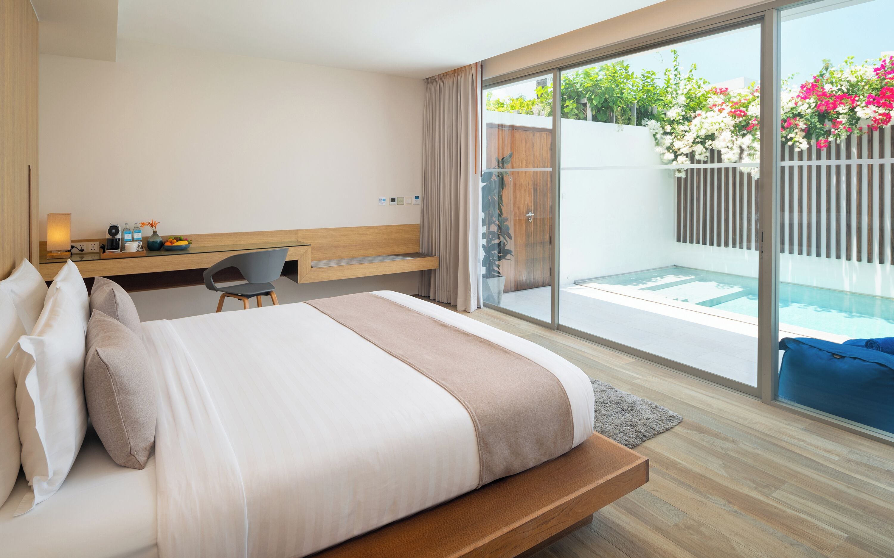 A modern hotel room with a large bed, a desk, and a view of a swimming pool and garden.