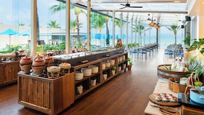 Un restaurante con mesas de buffet, mobiliario de madera y vista al océano.