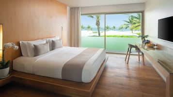 A hotel room with a large bed, a desk with a chair, a TV, and a view of the beach.