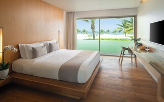 A hotel room with a large bed, a desk with a chair, a TV, and a view of the beach.