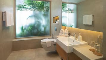 A modern bathroom with a large window, a bathtub, a sink with toiletries, and a toilet.