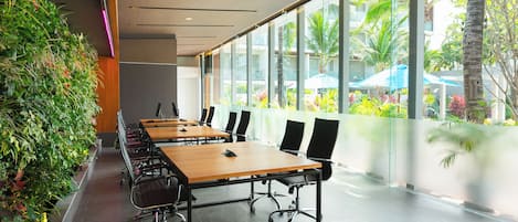 Una sala de conferencias con una larga mesa, sillas y un amplio ventanal con vistas a zonas verdes y un edificio.